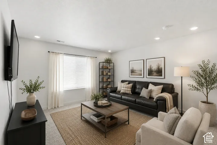 Recessed lighting illuminates this living area featuring a large window with blinds and sheer curtains, textured carpeting, and light gray wall finishes
