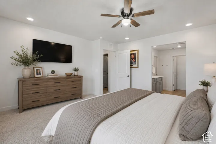 Carpeted bedroom featuring a ceiling fan with light fixture, recessed lighting, and an entryway to a bathroom with wood-finish flooring and a vanity with a sink