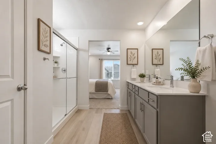 Bathroom featuring a dual vanity with grey cabinetry and light countertops, a large frameless mirror, and a glass-enclosed shower