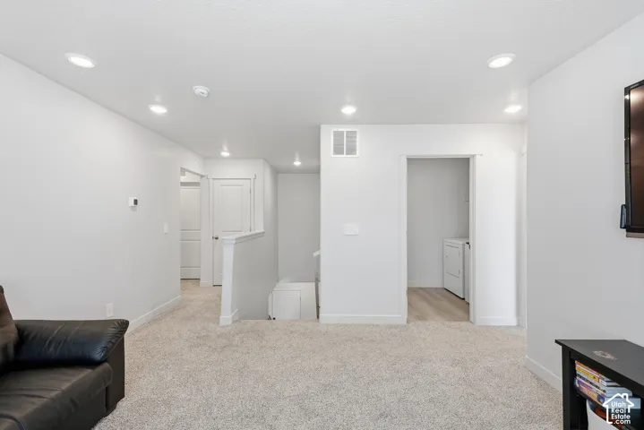 Carpeted area featuring recessed lighting, light gray wall paint, white trim, and a doorway revealing wood-finish flooring
