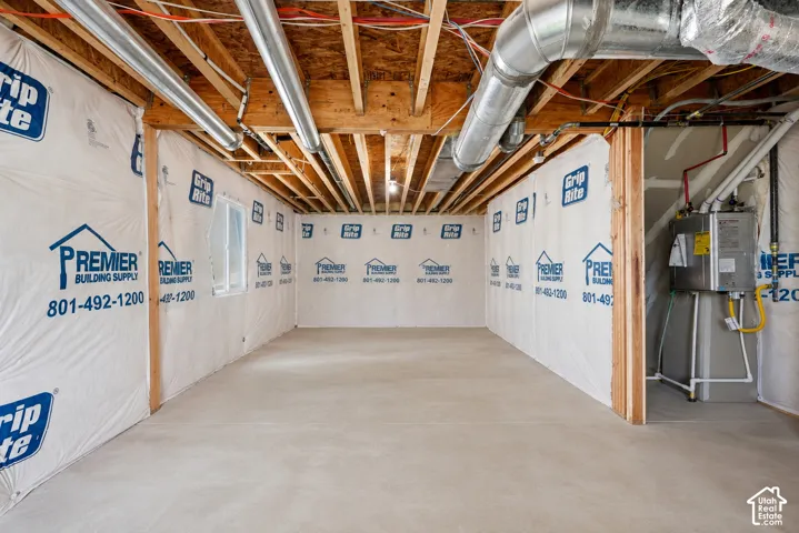 Unfinished basement with exposed ceiling joists and ductwork, featuring a poured concrete floor and a visible water heater installation
