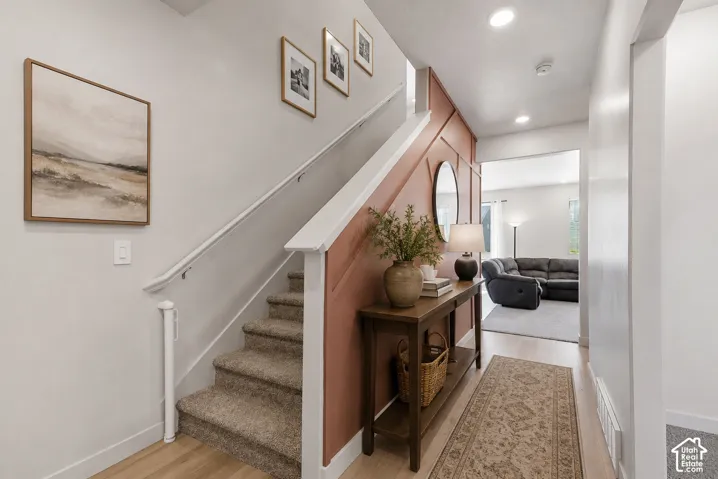 Entryway featuring wood-finish flooring, a carpeted staircase with white railing, and a feature wall with decorative paneling