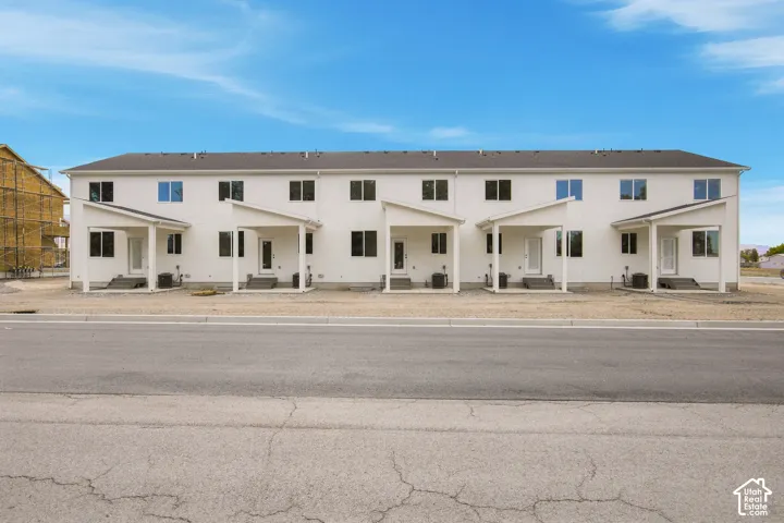 Newly constructed townhome community featuring contemporary white exteriors, covered patios, and dark-framed windows