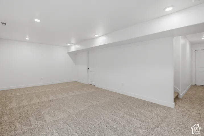 Spacious room featuring neutral carpeting, white walls, recessed ceiling lighting, and a white interior door