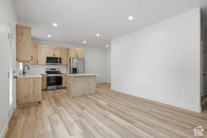 Kitchen featuring light wood-finish cabinetry, stainless steel appliances, a center island with countertop, and wood-finish flooring