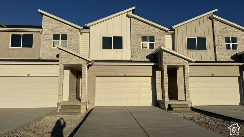 Contemporary townhome exterior featuring stone and vertical siding accents, a covered entry, and an integrated garage