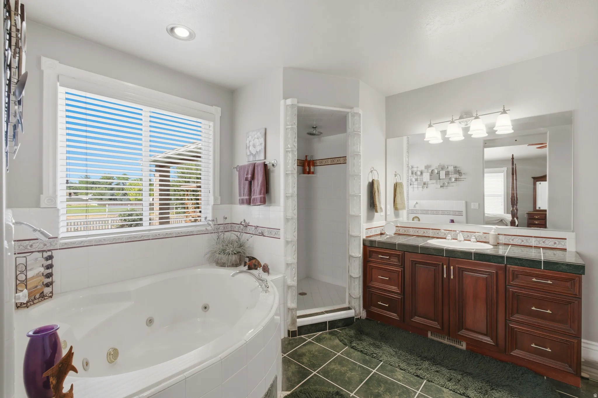 Bathroom featuring a corner jetted tub, a separate tiled shower, and a vanity with dual wood-finish cabinetry, a single sink, and a large mirror