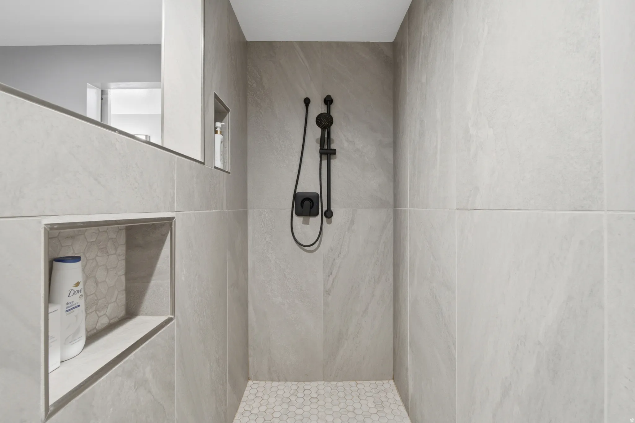 Walk-in shower with large format light gray wall tiles, hexagonal floor tiles, and matte black fixtures
