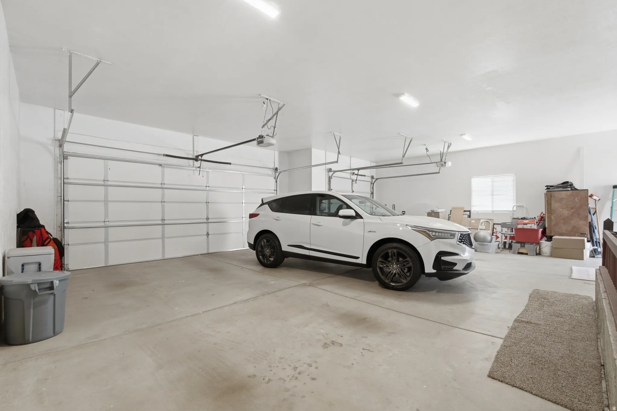 Two-car garage featuring concrete flooring, white paneled garage door, and overhead lighting