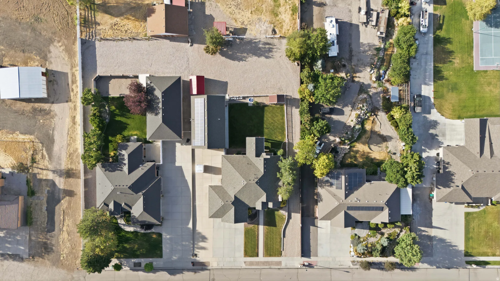 Aerial view showcasing multiple residential properties with dark shingle roofing, concrete driveways, and varied landscaping