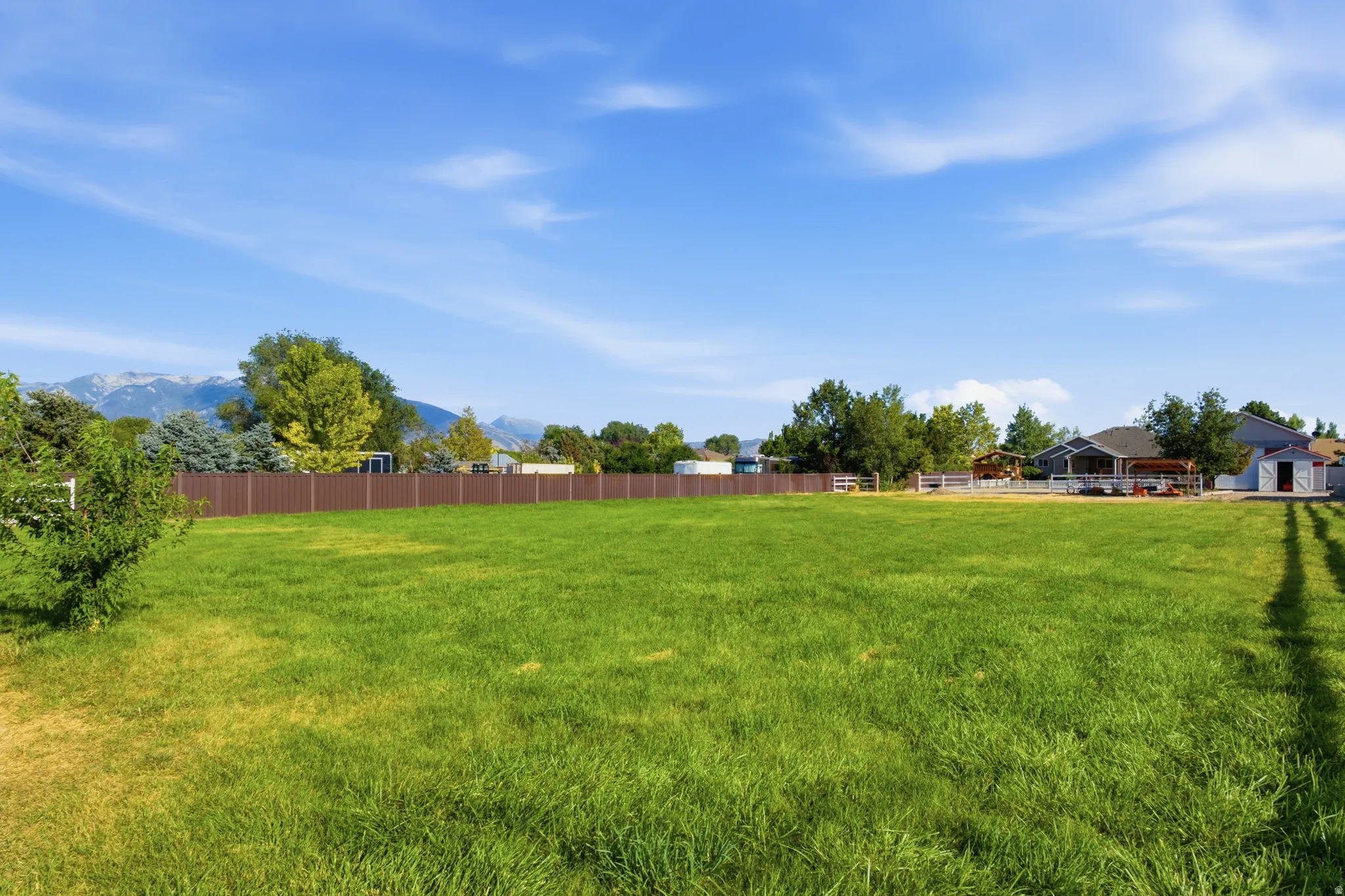 Expansive green space featuring a mountain backdrop, mature trees, and a perimeter fence