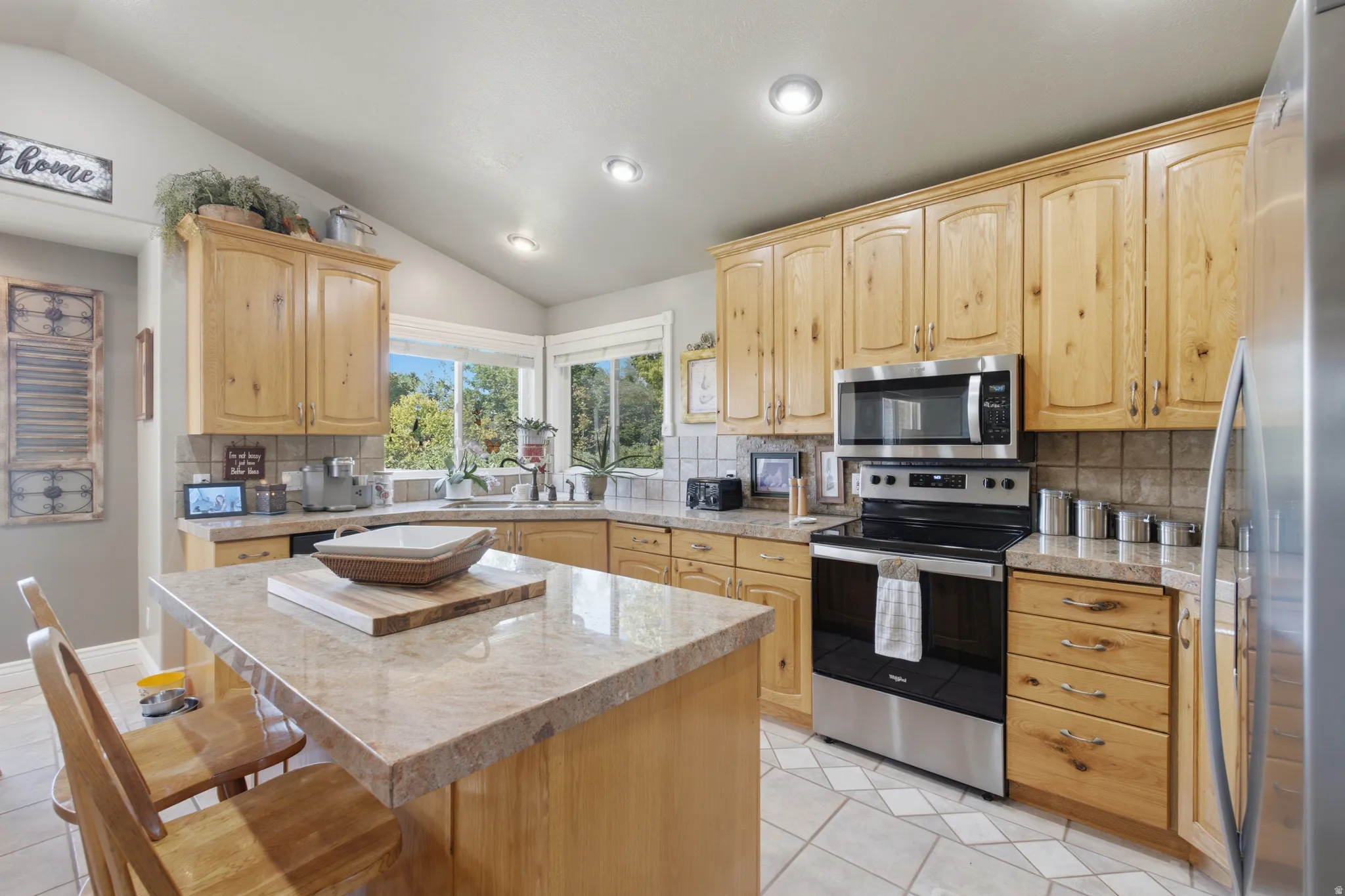 Kitchen featuring a central island with stone countertop, stainless steel appliances, light wood cabinetry, tile flooring, and a tiled backsplash