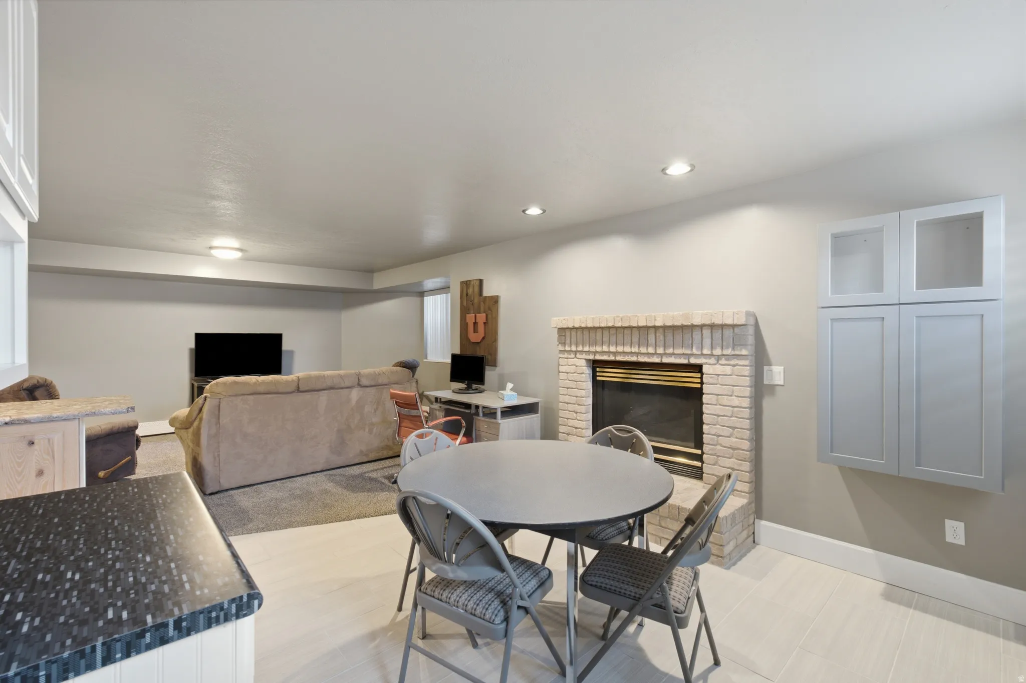 Open concept space featuring a light brick fireplace, recessed lighting, neutral wall tones, light wood-finish flooring, and built-in cabinetry