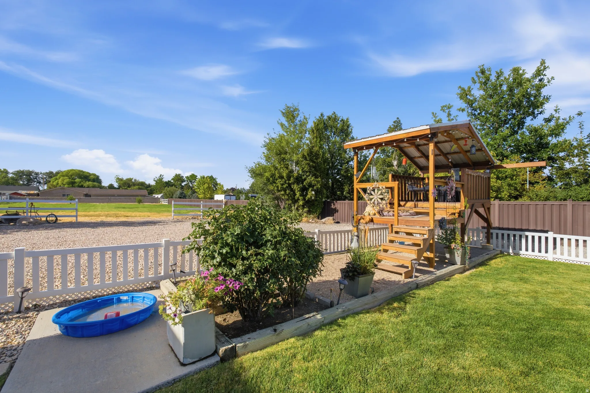 Expansive backyard featuring a lush lawn, white picket fencing, and a built-in wooden play structure with a metal roof