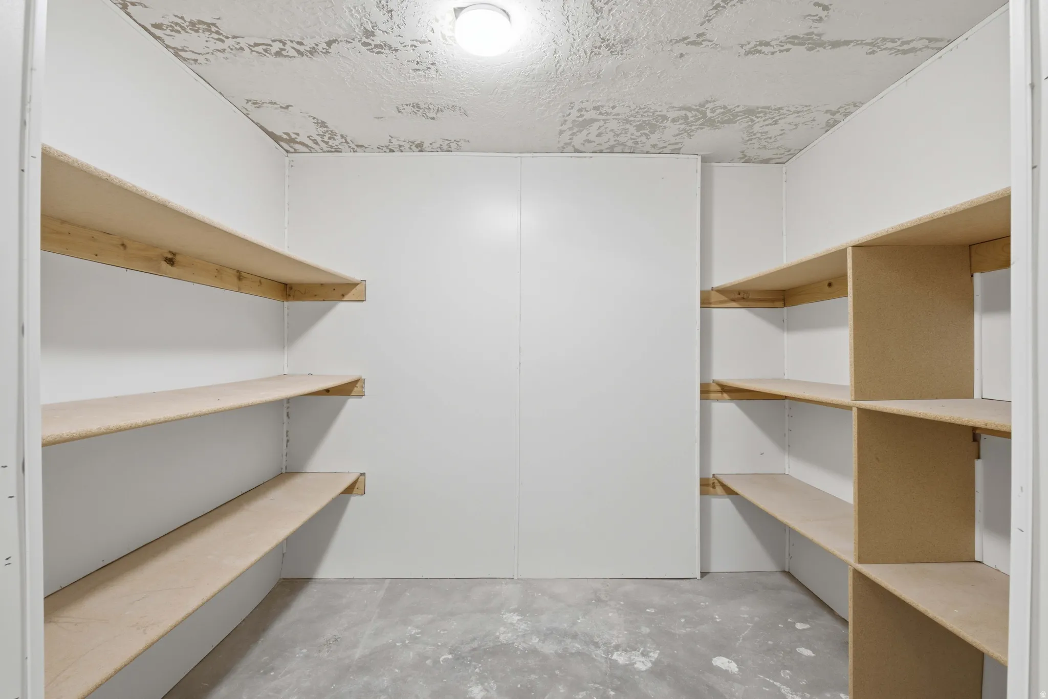 Dedicated storage room featuring multiple built-in shelving units, a concrete floor, painted white walls, and an overhead light fixture