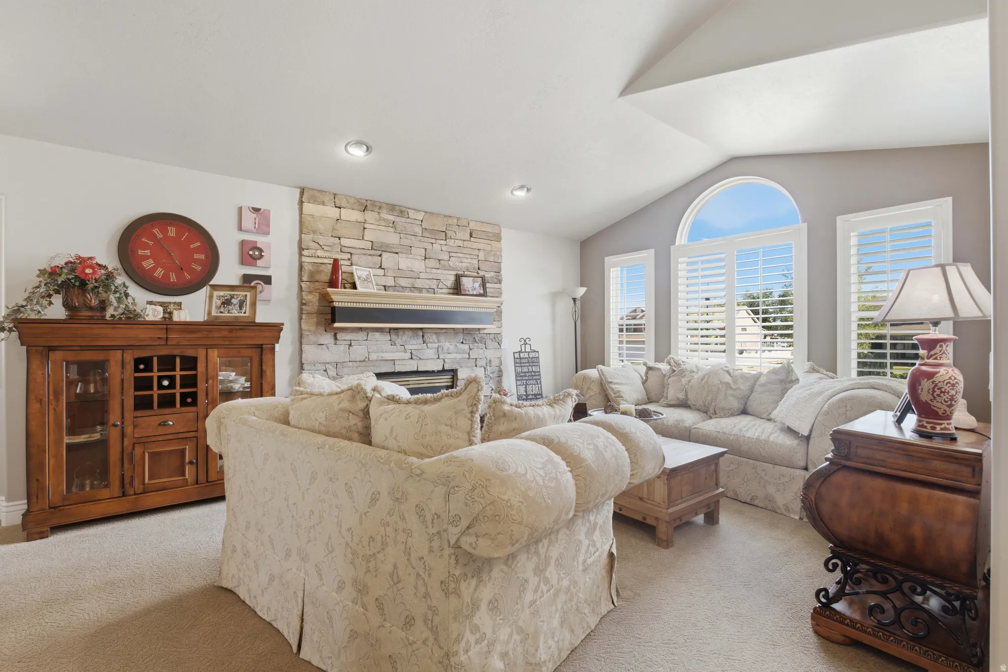 Living room featuring a stone fireplace with a wood mantle, vaulted ceilings, and recessed lighting