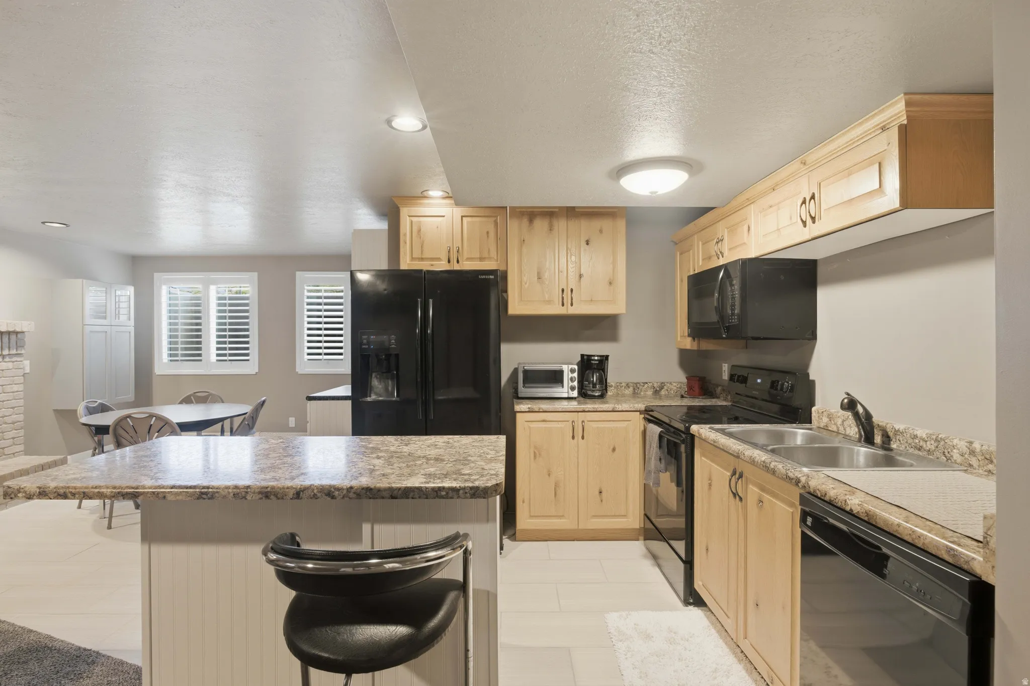 Kitchen featuring light wood cabinetry, black appliances, light-toned countertops, and an island with bar seating