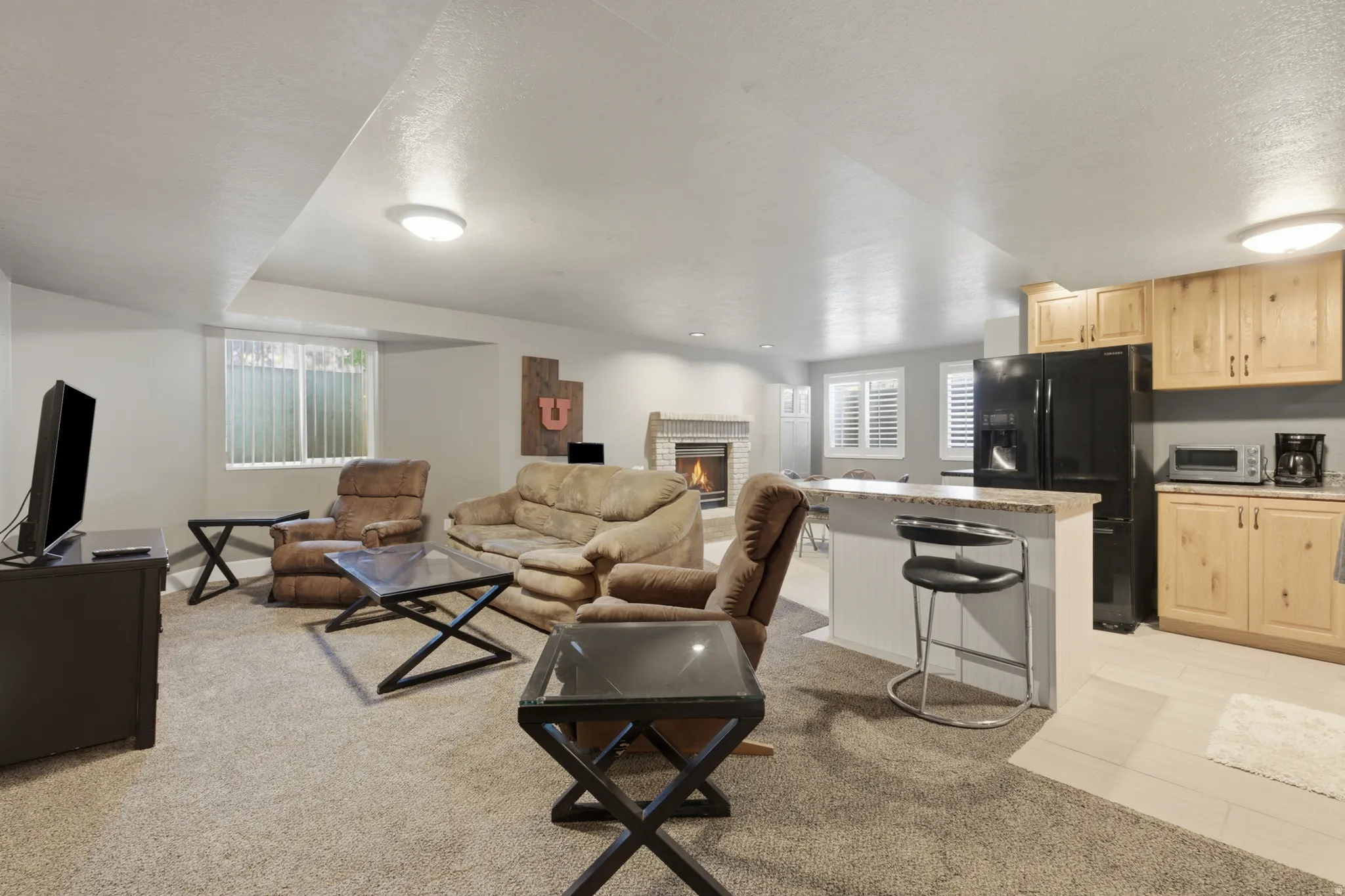 Open-concept living space featuring a built-in fireplace with a stone surround, a kitchen area with wood cabinetry and a breakfast bar, recessed lighting, and carpeted flooring