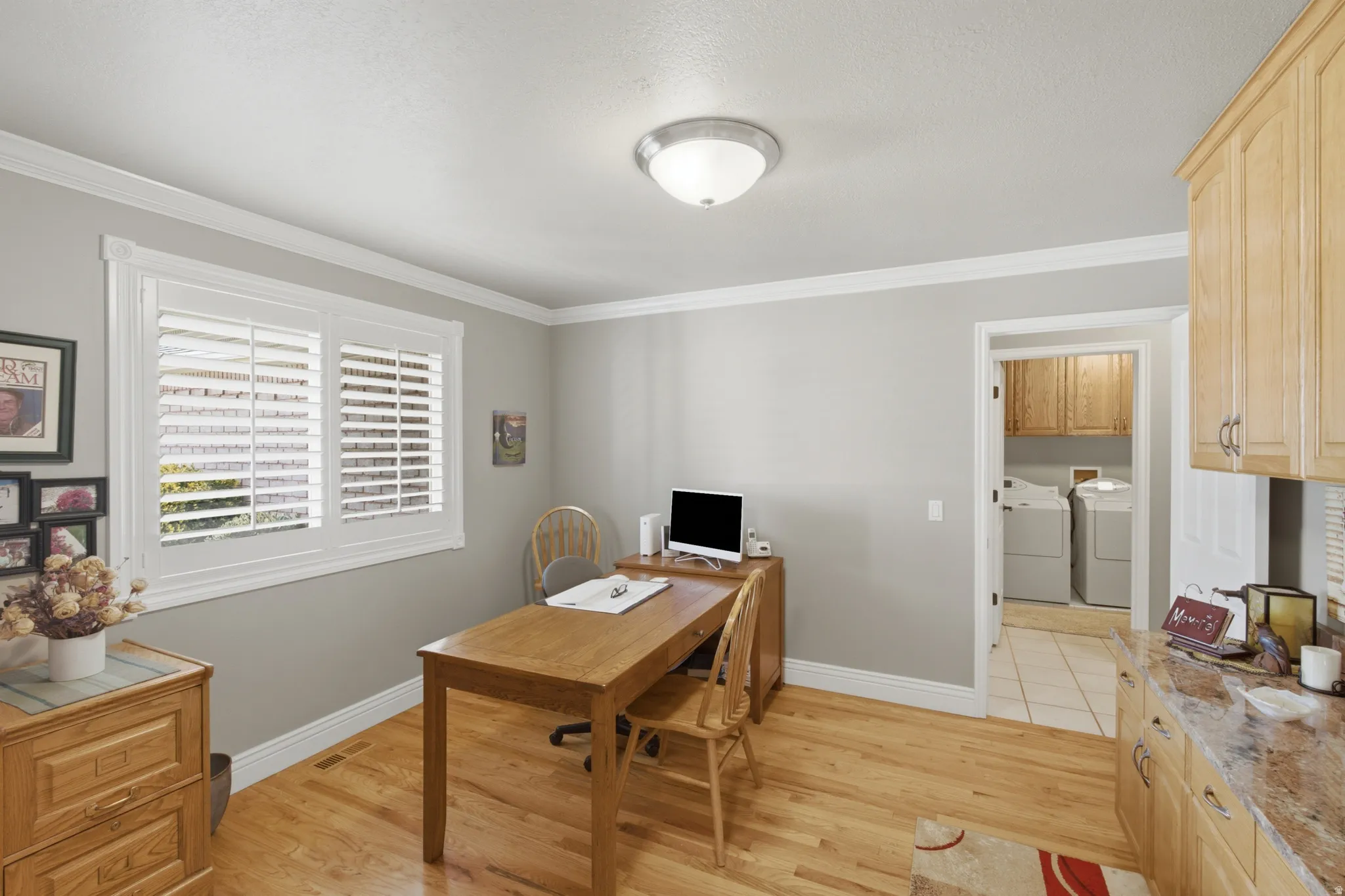 Hardwood flooring extending into a doorway, featuring a window with white plantation shutters, light gray walls, and white crown molding