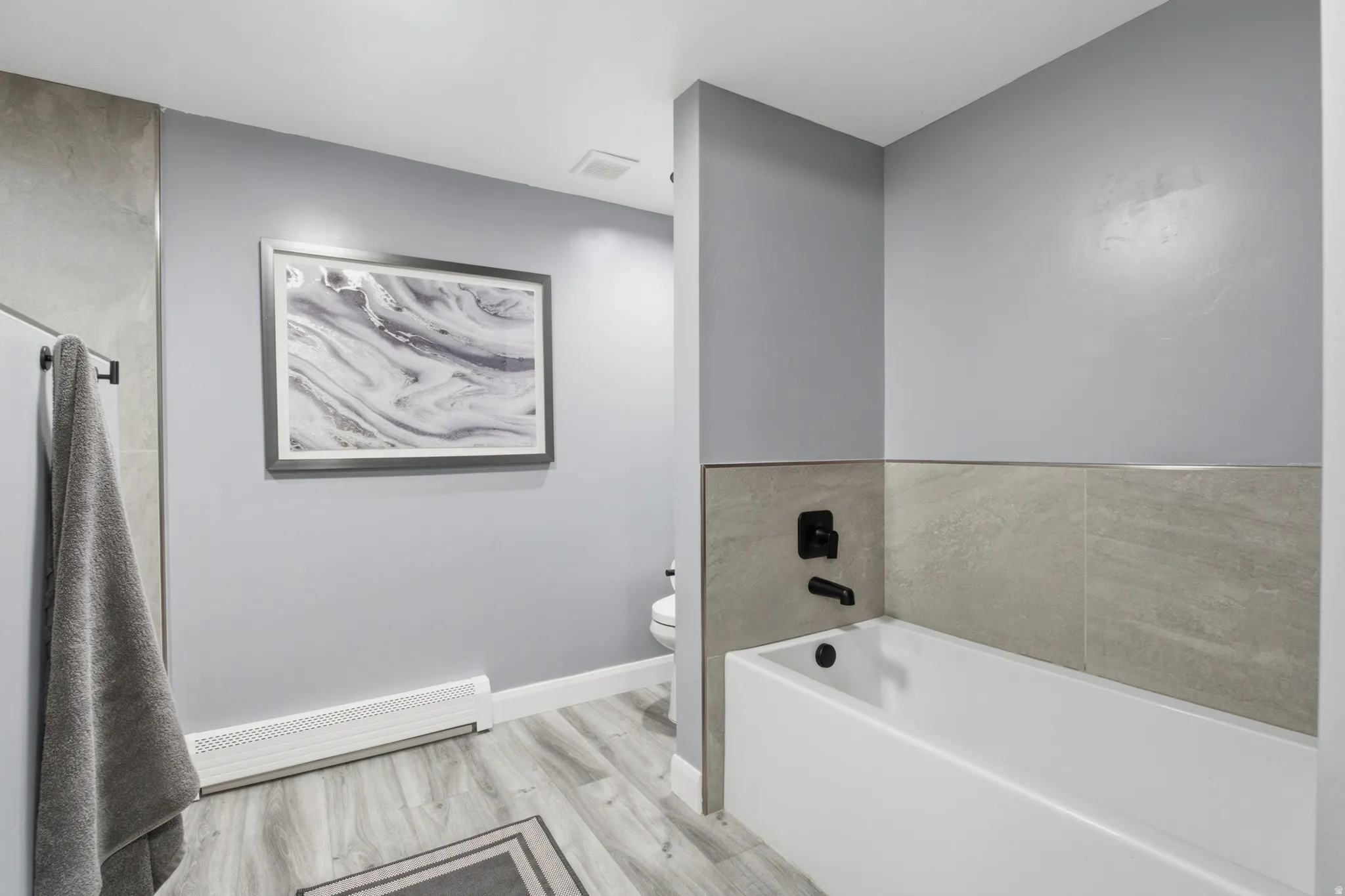 Full-size bathtub with matte black fixtures and light gray tile surround, set against a light gray wall