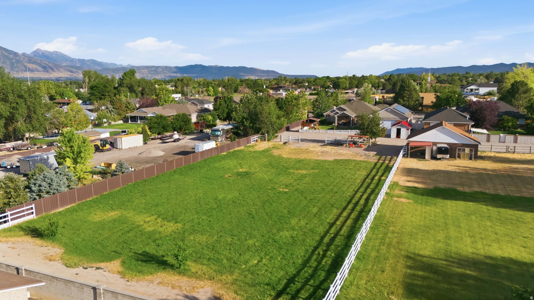 Expansive green space featuring a white split-rail fence and a brown privacy fence