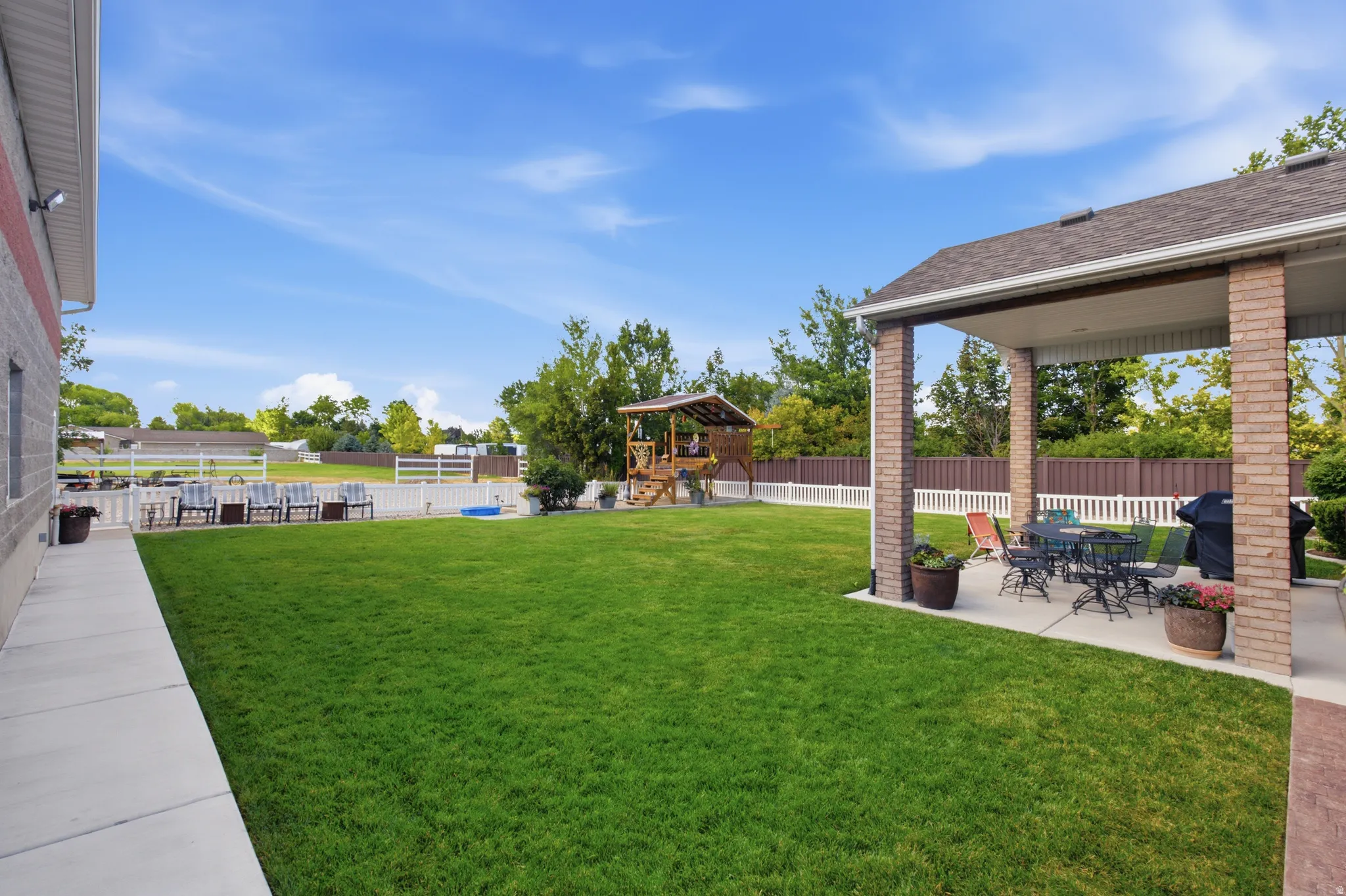 Expansive green lawn with a covered patio, brick columns, and a partial white picket fence