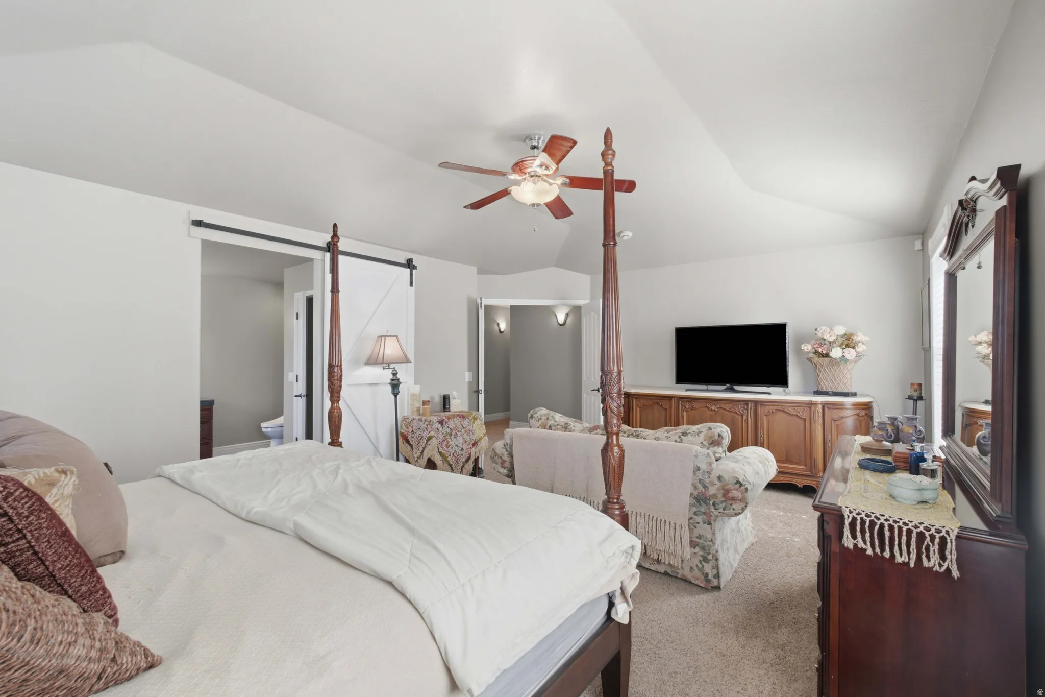 Spacious room featuring vaulted ceilings, a ceiling fan, carpet flooring, and a white barn door