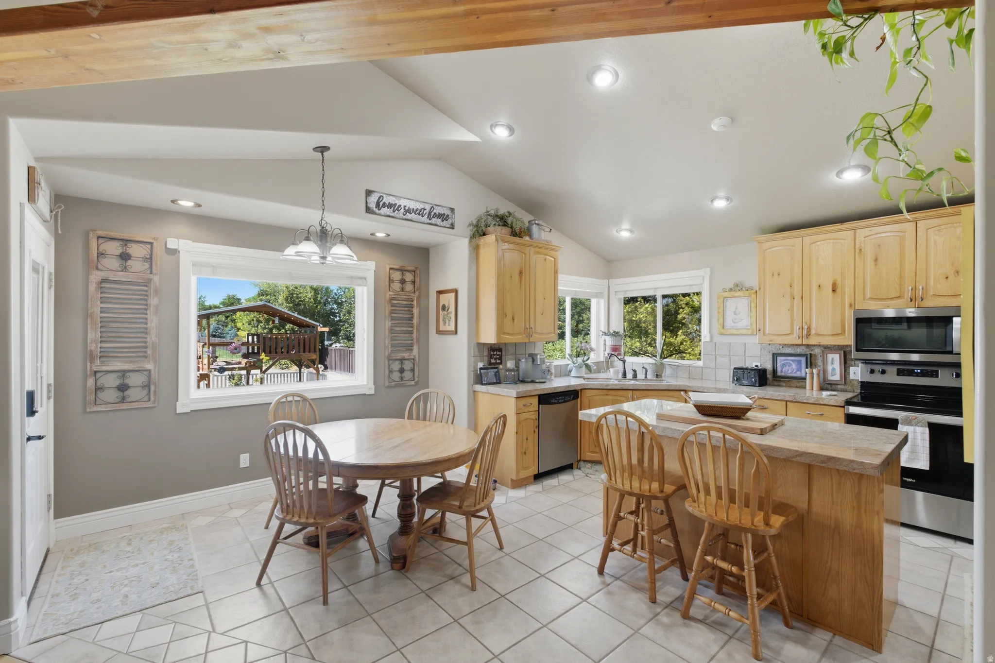 Spacious kitchen featuring light wood cabinetry, stainless steel appliances, a central island with wood-finish countertop, and tile flooring