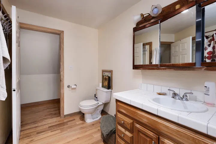 Bathroom featuring wood-finish flooring, a white tiled countertop, a recessed medicine cabinet with wood trim, and a white toilet