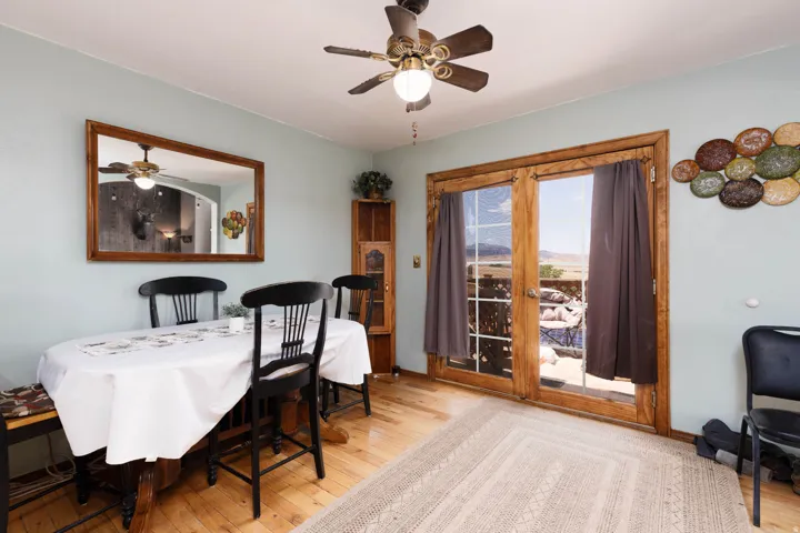Wood-finish flooring with a ceiling fan overhead, featuring French doors with wood frames and a wide outdoor landscape