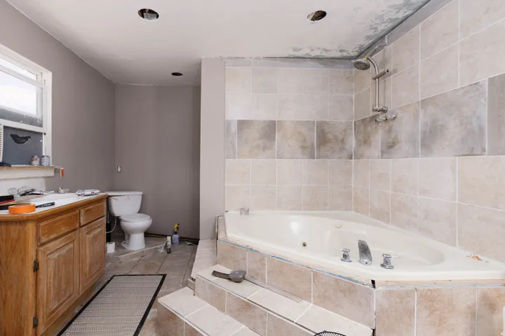 Bathroom featuring a corner jetted tub with tiled surround, a tiled shower with a handheld showerhead, a wood-finish vanity with a white countertop, and recessed lighting