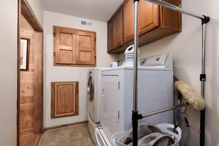 Dedicated laundry area featuring a washer and dryer, upper and lower wood cabinetry, and a wood-paneled doorway