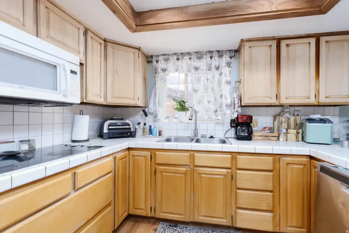 Kitchen featuring wood cabinetry, white tile countertops, a white tile backsplash, an undermount double basin sink, and wood-finish flooring