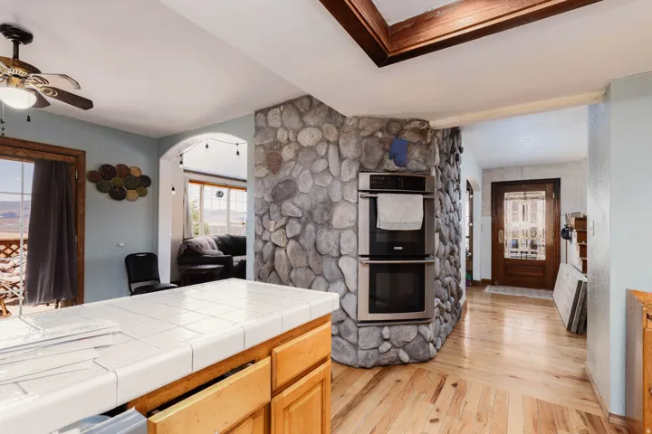 Kitchen featuring a tile-top island, wood-finish flooring, and built-in stainless steel double ovens integrated into a stone-clad wall