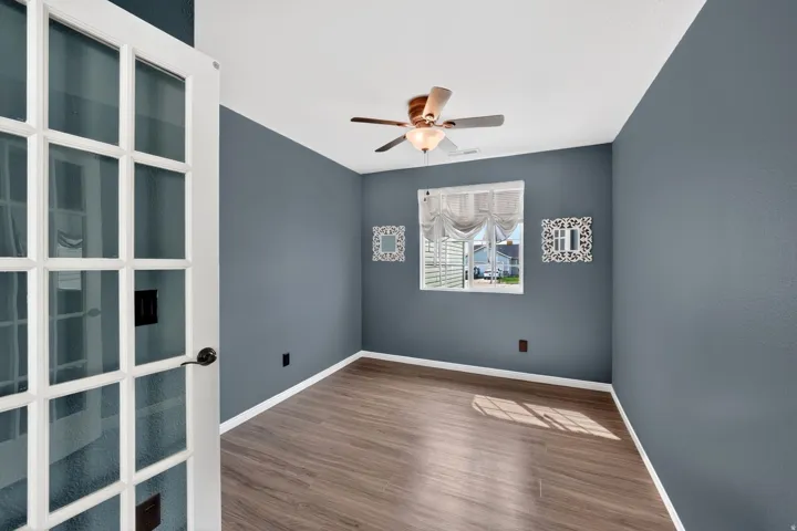 French doors open to a versatile room featuring wood-finish flooring, a ceiling fan with light fixture, and a window with blinds