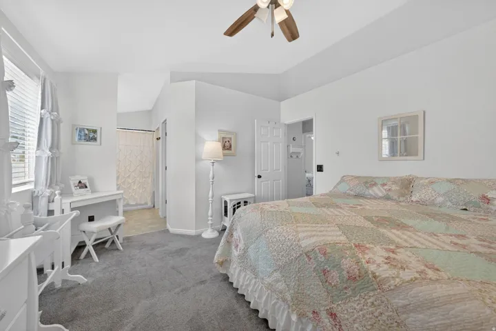 Spacious bedroom featuring vaulted ceilings, a ceiling fan with light fixture, gray carpeting, and a window with blinds