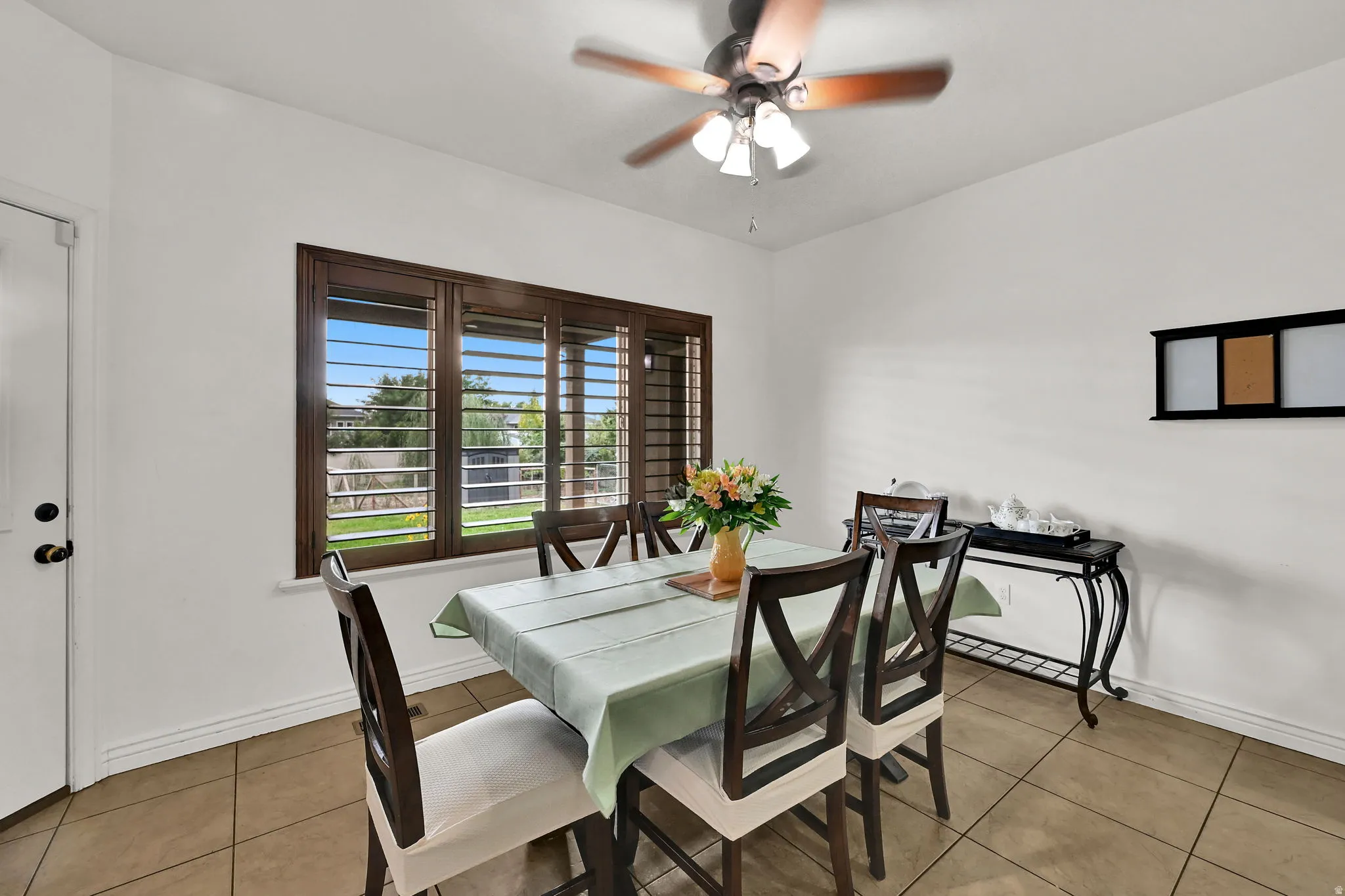 Spacious dining area featuring a ceiling fan, tile flooring, and a large window with louvered shutters