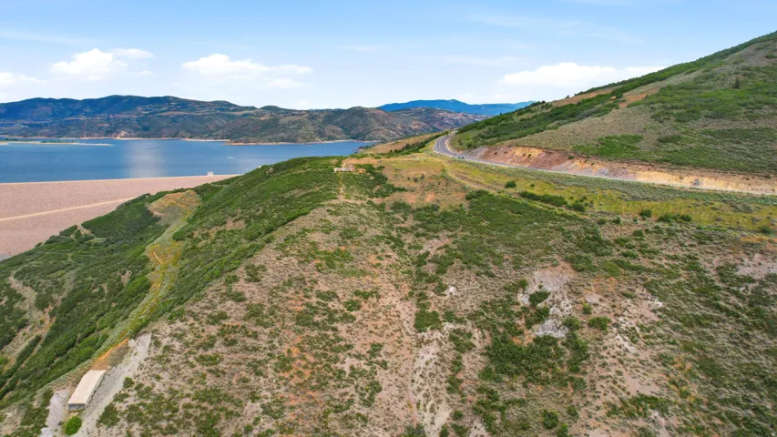 Mountainous terrain with a winding road overlooking a large body of water and a substantial dam structure