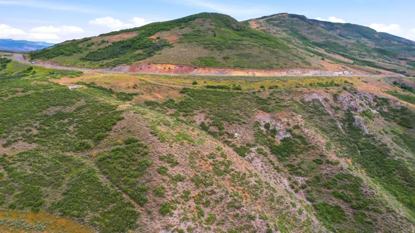 Rolling hills of natural terrain with a winding road across the hillside, featuring expansive natural vegetation and distant mountainous topography