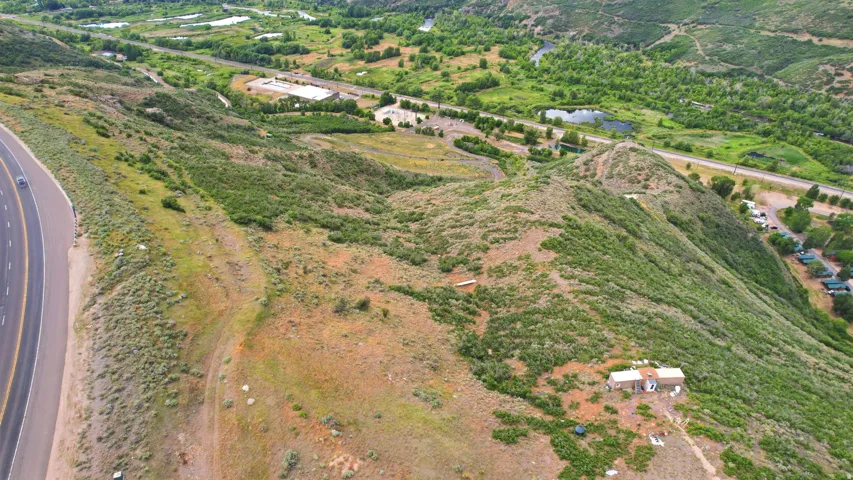 Expansive hillside property featuring diverse vegetation, a visible roadway, and distant green landscape with water features