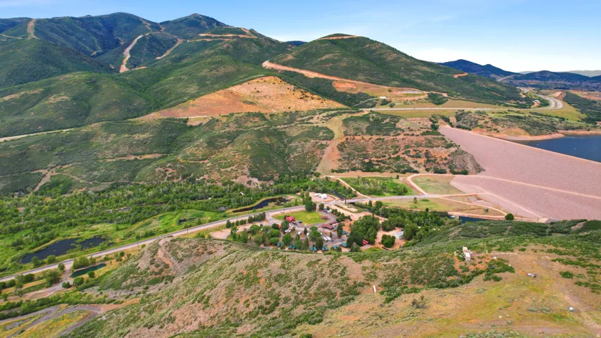 Expansive mountain landscape featuring a large body of water, a prominent dam, and a collection of structures
