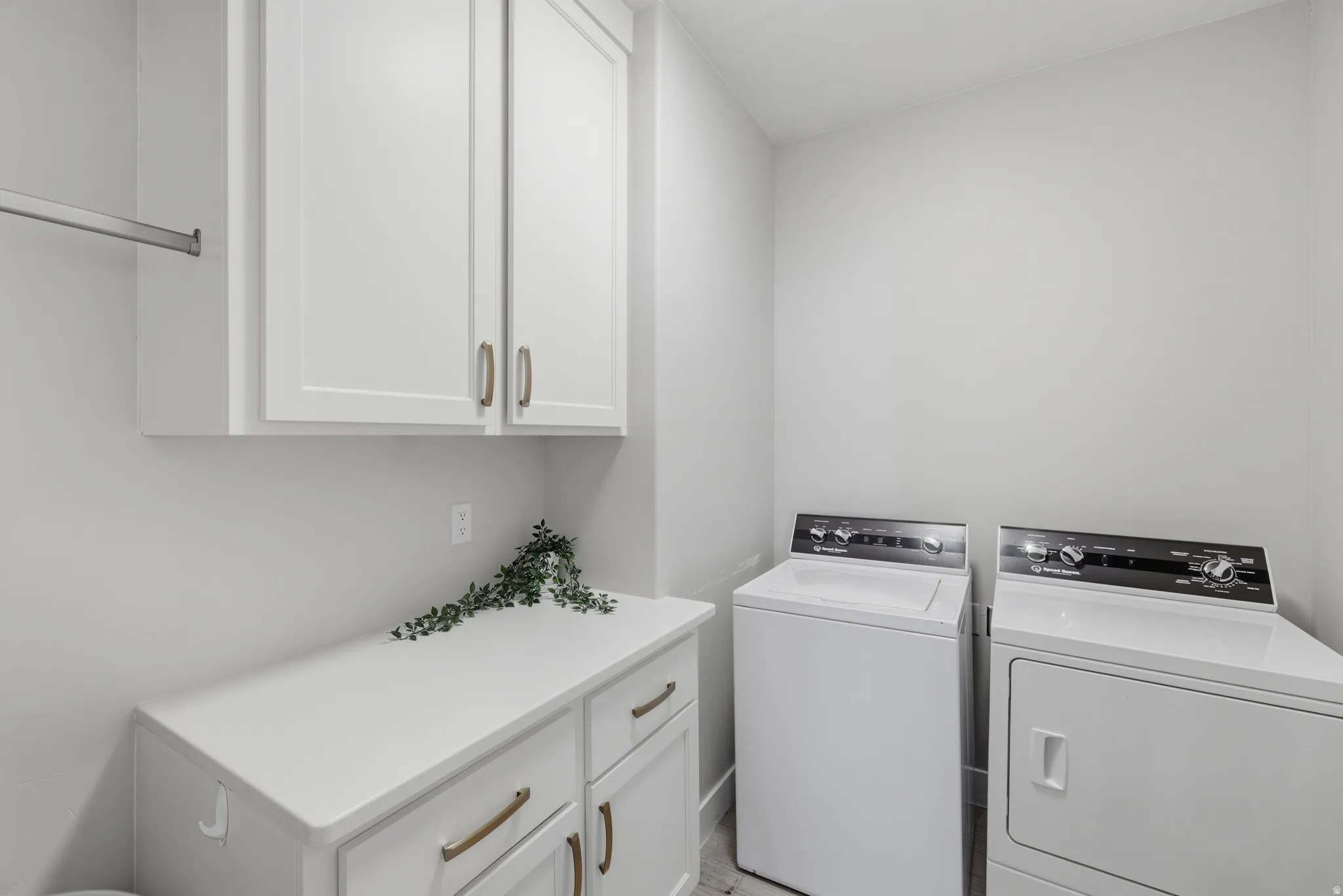Dedicated laundry area featuring white shaker-style cabinetry with bronze hardware, a white countertop, and a metal hanging rod