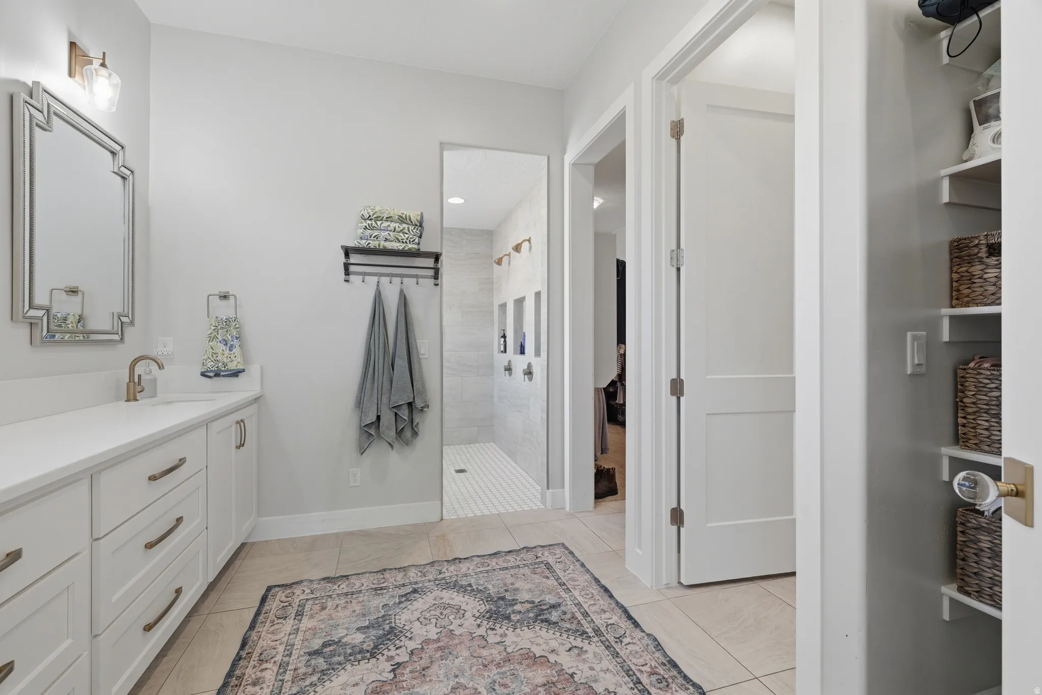 Modern bathroom featuring a single vanity with a white countertop and bronze hardware, framed mirror, and a tiled walk-in shower with multiple showerheads