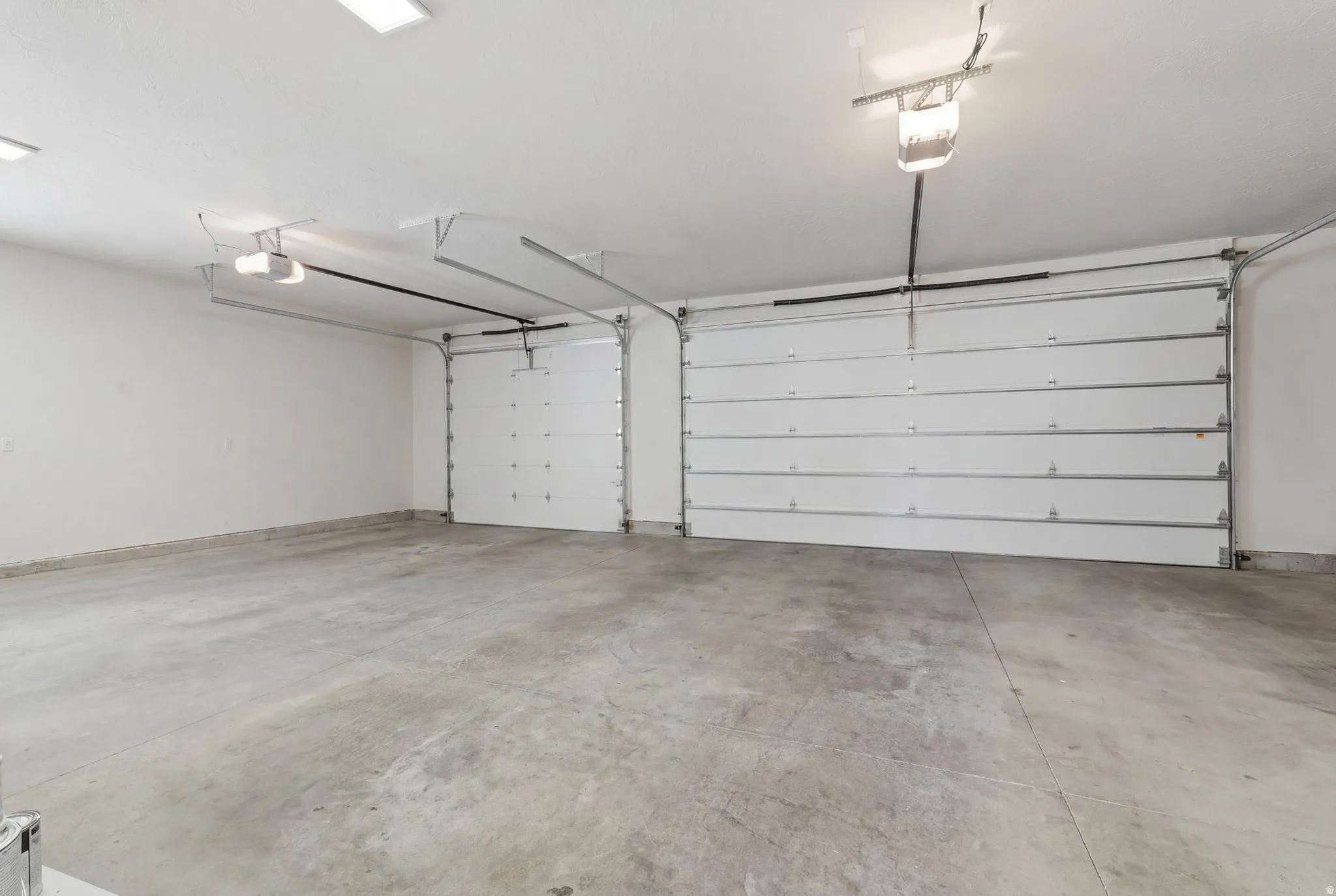 Spacious garage featuring a concrete floor, two white overhead doors with openers, and overhead lighting