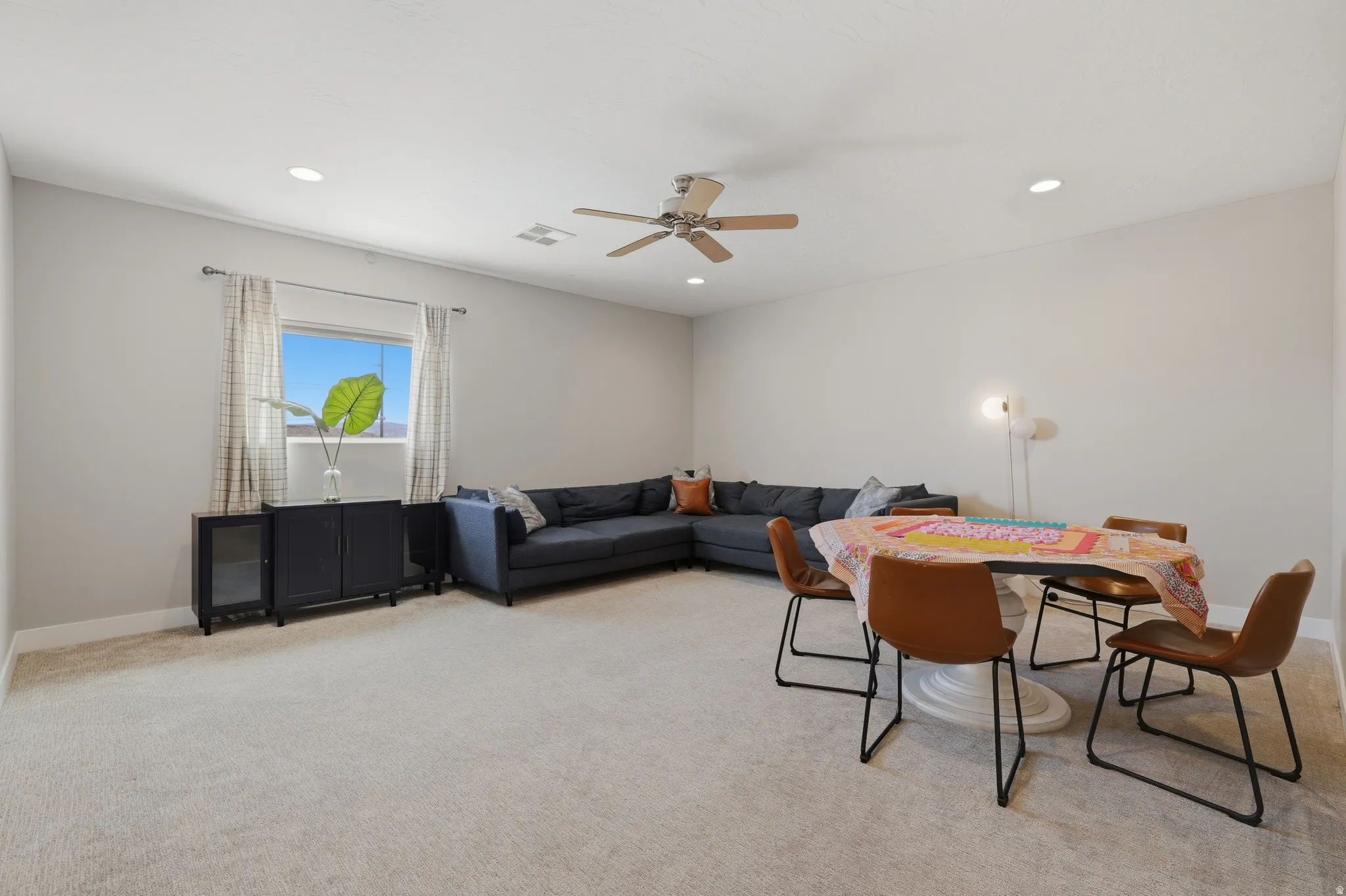 Spacious carpeted room featuring a window with patterned drapes, recessed lighting, and a ceiling fan
