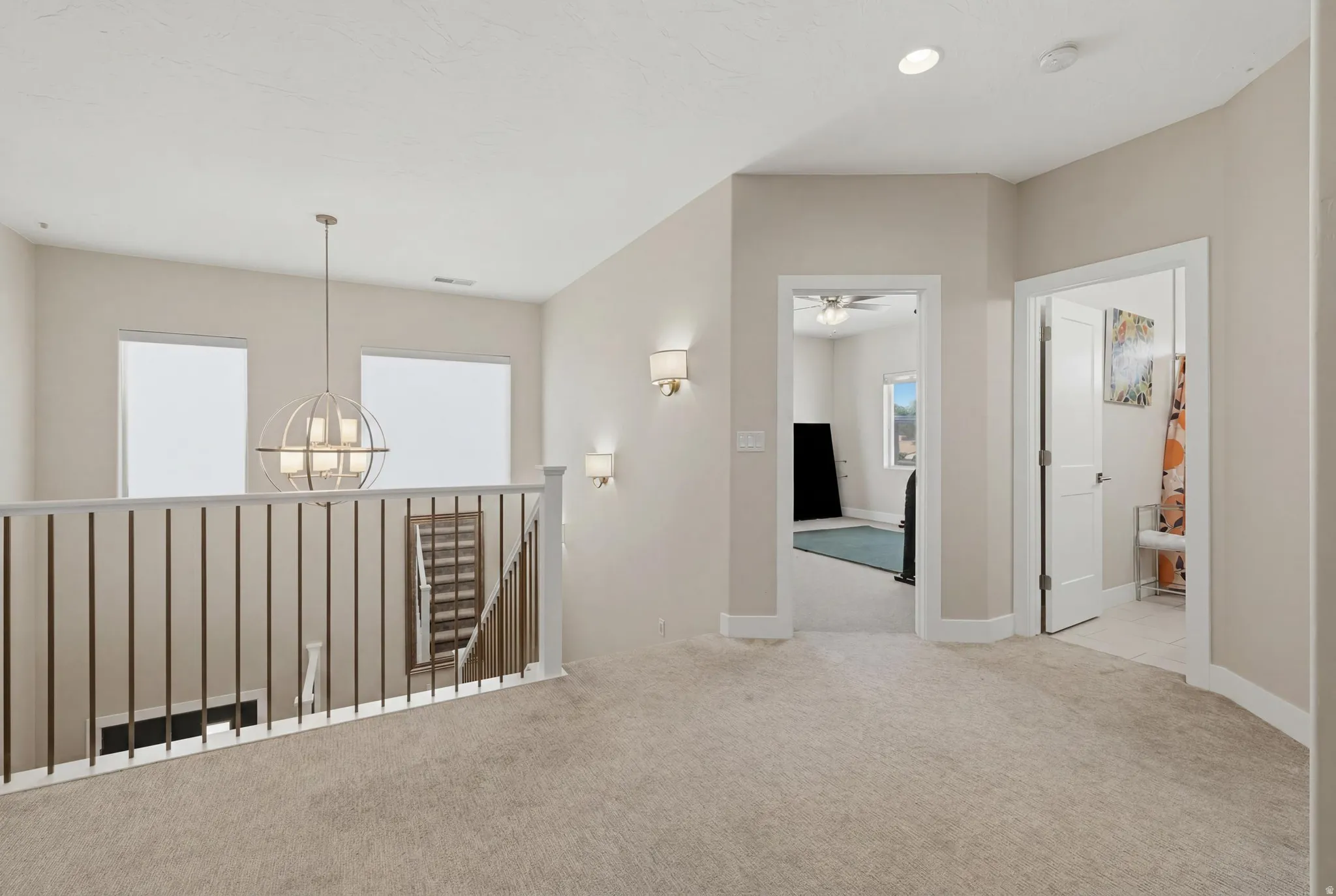 Upper-level hallway featuring neutral carpeting, a contemporary chandelier, two wall sconces, and multiple doorways leading to additional rooms