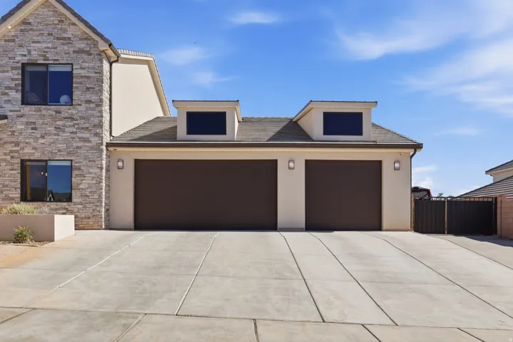 Exterior with stacked stone facade and stucco finish, featuring a concrete driveway, two brown garage doors, and two dormer windows