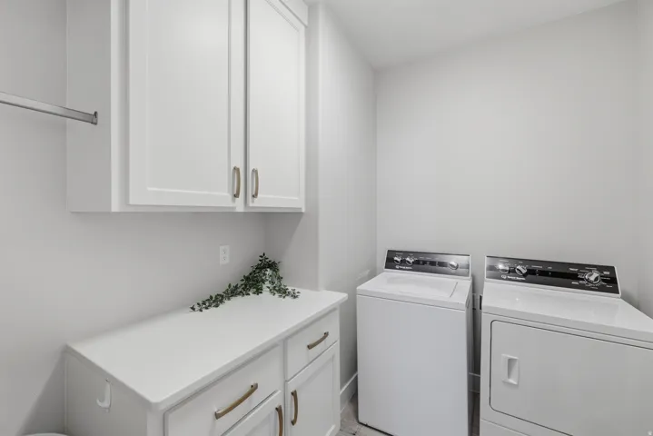 Dedicated laundry area featuring white shaker-style cabinetry with bronze hardware, a white countertop, and a metal hanging rod
