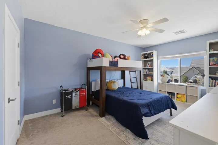 Bright room featuring a large window, light-colored carpet, a ceiling fan, and built-in shelving