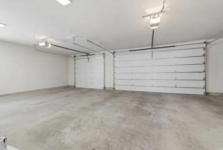 Spacious garage featuring a concrete floor, two white overhead doors with openers, and overhead lighting